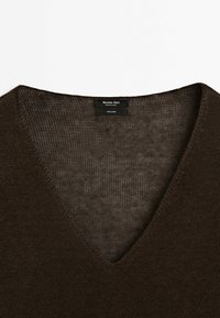 Pull en lin tricoté marron foncé à col en V avec texture visible et une étiquette noire indiquant "Massimo Dutti, Made in China, 100 % lin."