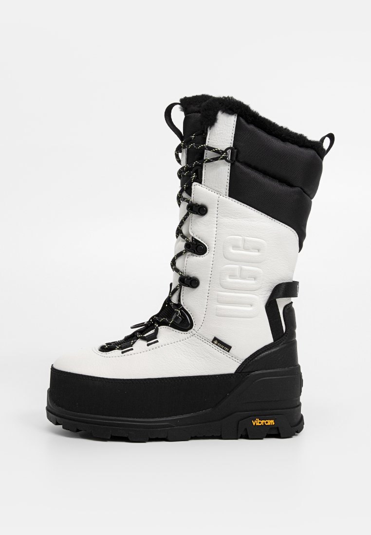 Hohe Schnür-Winterstiefel aus schwarz-weißem wasserdichtem Leder, mit schwarzer Fellinnenausstattung, gebrandetem UGG-Seitenlogo und Vibram-Gummisohle.