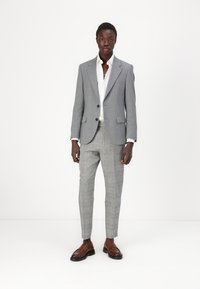 Sacou gri personalizat cu două nasturi, cămașă albă și pantalon gri în carouri. Pantofi de piele maro completează ținuta.