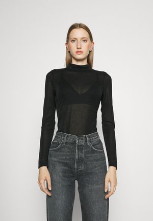 Mustapaita, jossa on pitkä hihainen poolo ja läpinäkyvä, hieman teksturoitu pinta; yhdistettynä korkeavyötäröisiin, tummanharmaisiin farkkuihin, joissa on klassiset denim-yksityiskohdat.