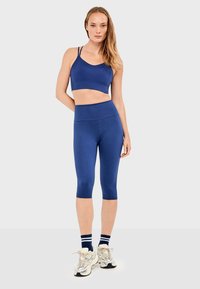 Conjunto deportivo azul marino que incluye una camiseta corta con tirantes finos y leggings tipo capri ajustados de talle alto.