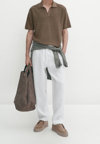 Polo shirt marron à côtes, pantalon blanc, pull gris noué à la taille, sac en daim marron et chaussures marron clair. Design minimaliste.