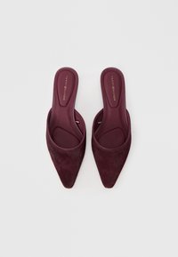 Burgundijas krāsas norādītas mules ar mīkstu, teksturētu audumu un gludu iekšējo oderi. Funkcijas diskreta zīmola identificēšana uz zolītes.