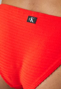 Červené pruhované bikiny s čiernou obdĺžnikovou nášivkou CK; hladký materiál s vysokým pásom.