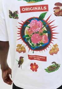 Hvid bomulds T-shirt med farverige grafikker af blomster, sommerfugle og dyr, med teksten "ORIGINALS" og "CRAFTED AESTHETICS EST.1990".