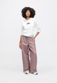 Hellgrauer Hoodie mit einer Fronttasche und Logo, kombiniert mit locker sitzenden, hoch taillierten, hellrosa Satin-Hosen und weißen Turnschuhen.