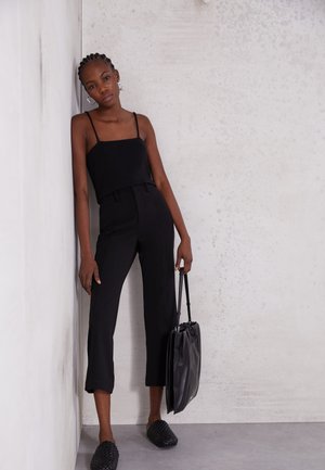Top de malha preto com riscas, com alças finas, calças pretas de cintura alta, sapatos slip-on pretos de trama e uma mala de mão preta em couro.