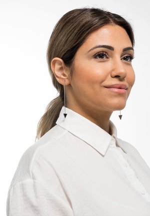 Orecchini in filo d'argento con accenti neri a forma triangolare; design minimalista, forma allungata. Indossati da un modello con capelli di lunghezza spalla e una camicia con colletto.