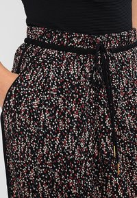 Mustat kukkahousut, joissa pieni punainen ja valkoinen kukkakuvio, pehmeä kangas, joustava vyötärönauha kiristysnauhalla ja sivutaskut.