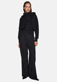 Maglione nero lavorato a maglia con dettaglio a collo drappeggiato e testurizzato, abbinato a pantaloni neri a gamba larga. Tessuto liscio e design minimalista.