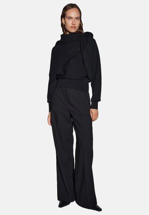 Zwarte gebreide trui met een gestructureerd, gedrapeerd neklapje, gecombineerd met een zwart broek met wijde pijpen. Glad materiaal en minimalistisch ontwerp.