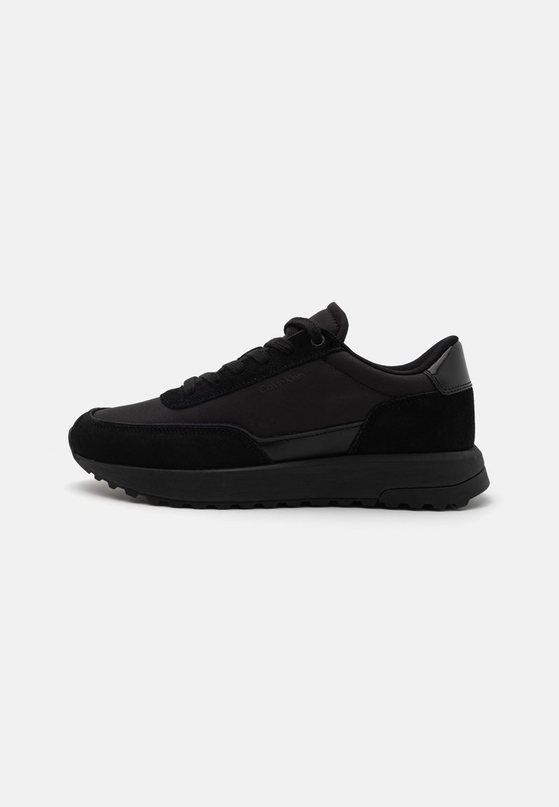 Zwarte sportschoenen met een combinatie van glad synthetisch materiaal en geperforeerd suede, voorzien van een rubberen zool en vetersluiting.