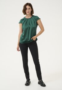 Green satin blouse with short sleeves and pleat detailing, paired with black skinny jeans and black patent loafers.