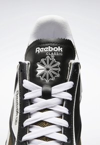 Černobílý teniska Reebok Classic s texturovaným koženým svrškem, bílými tkaničkami a logem s motivem hvězdného výbuchu.