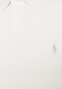 Beige polo shirt made of textured fabric, featuring a three-button placket and an embroidered logo on the left chest.