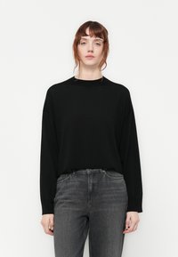 Top nero a maniche lunghe con collo alto. Realizzato in tessuto morbido, presenta una vestibilità comoda e cuciture delle spalle scese. Abbinato a jeans grigio scuro.