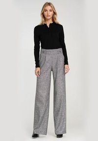 Spodnie o wysokim stanie i szerokich nogawkach w szarym wzorze w kratę houndstooth, z teksturowanym materiałem i dużymi przednimi kieszeniami. W zestawie z czarną bluzką.