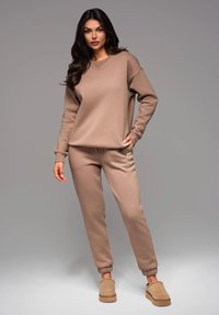 Beige Sweatshirt und passende Jogginghose aus weichem Stoff, mit lockerem Schnitt, gerippten Bündchen und einem kleinen Logo-Schriftzug auf der Hose.