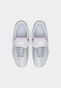 Ζευγάρι ασημένια παπούτσια ποδοσφαίρου Puma King με κορδόνια και αναδιπλούμενη γλώσσα που δείχνει το λογότυπο Puma, εμφανιζόμενα από πάνω σε λευκό φόντο.