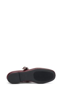 Zapato de cuero burdeos con punta redondeada, acento de hebilla y suela de goma negra texturada, diseñado para soporte y comodidad.