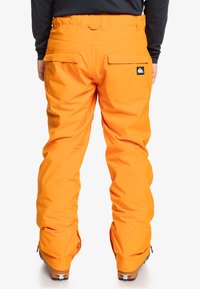 Pantalones de nieve naranjas con un corte holgado, fabricados con material impermeable. Cuentan con dos bolsillos traseros y dobladillos reforzados para mayor durabilidad.