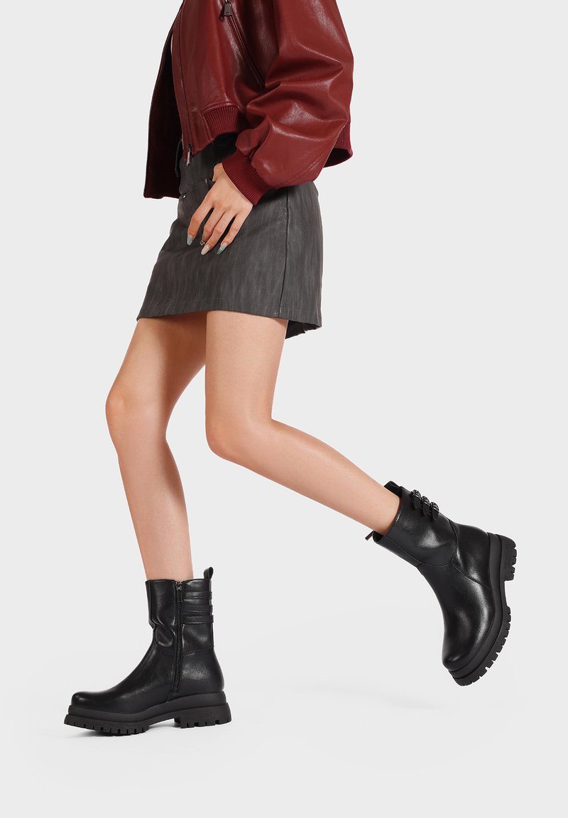 Stivaletti neri in pelle con una texture liscia, punta rotonda, cerniera laterale e tre cinture decorative nella parte superiore. Suola con battistrada spesso.