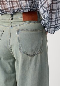 Lyseblå denimjeans med en avslappet passform, med brun lær-label merket "MADS NØRGAARD" og standard baklomme-design.