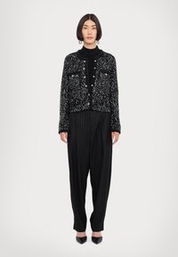 Giacca nera con decorazioni in paillettes e chiusura con bottoni, abbinata a un dolcevita nero, pantaloni a righe con gamba larga e décolleté a punta.