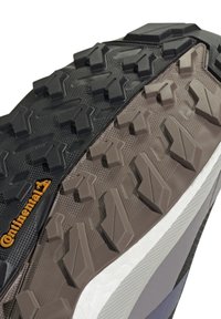 Gros plan d'une semelle de chaussure avec des crampons en caoutchouc noirs et marron robustes et le logo de la marque Continental en orange sur la partie noire.