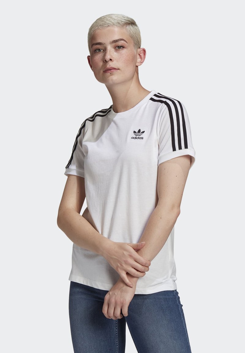 Balta medvilninė marškinėliai su juodomis trimis juostelėmis rankovėse, ant krūtinės esantis mažas juodas adidas logotipas. Sukrautos rankovės, laisvas siluetas.