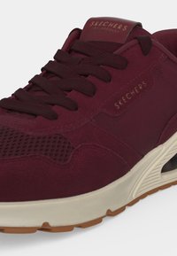 Крупен план на бордо маратонка Skechers с текстуриран мрежест материал, връзки отпред и бежова подметка с кафява шарка.