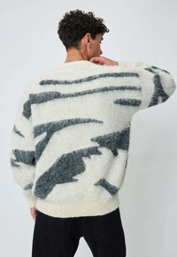 Pull en laine blanc et gris avec un motif abstrait, présentant une coupe ample, des poignets côtelés et une bande unie à l'ourlet.