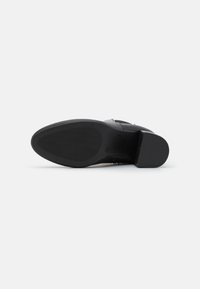 Schwarzer Lederschuh mit flacher Sohle, strukturiertem Gummiboden und breitem Absatz. Besitzt minimale Hardware und eine glatte Oberfläche.