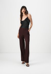 Schwarzes Satin-Camisole mit verstellbaren Trägern, kombiniert mit hochgeschnittenen burgunderfarbenen Hosen mit maßgeschneiderter Passform und Taschen. Schwarze Sandalen.