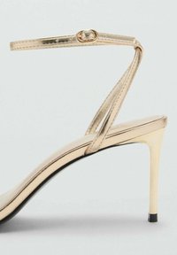 Metallic gold stiletto sandals with a thin ankle strap, open toe, and a glossy finish. Features a slim high heel and sleek design.