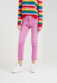 Jeans de mezclilla rosa ajustados y recortados con un dobladillo deshecho. Combinados con zapatillas blancas y un suéter de punto a rayas multicolores.