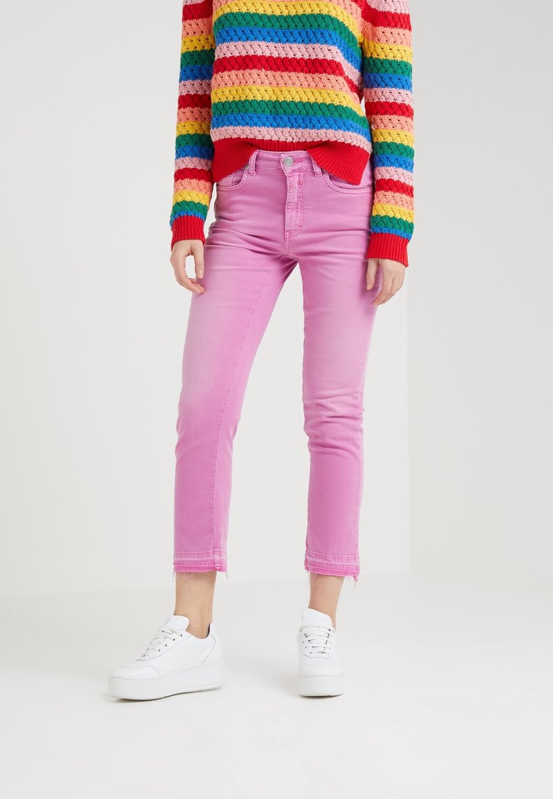 Jeans de mezclilla rosa ajustados y recortados con un dobladillo deshecho. Combinados con zapatillas blancas y un suéter de punto a rayas multicolores.