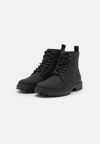 Botas negras hasta el tobillo, hechas de un material texturizado, con punta redonda, cordones y suelas de goma con tacos profundos para un mejor agarre.