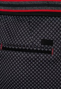 Tejido negro con un patrón de corazones en gris. Una cinturilla de rayas horizontales en colores rojo y negro. Incluye un pequeño detalle de bolsillo negro.