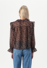 Blusa nera trasparente con motivo floreale rosa, colletto arricciato e maniche a campana. Abbinate a jeans in denim blu a vita alta.