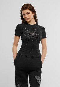 Kortermet svart t-skjorte med sommerfugldesign pyntet med rhinestones og stjerne mønster, laget av myk bomull.