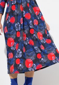 Robe florale avec un fond marine, ornée de cercles rouges et de fleurs bleues, fabriquée dans un tissu à la texture lisse et au design fluide.