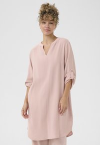 Tunic roz deschis dintr-un material texturat, cu decolteu în V, mâneci răsfrânte și o croială relaxată, cu slituri laterale.