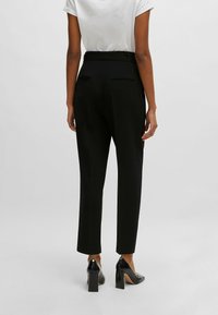 Svarta skräddarsydda byxor med smal passform och mjukt tyg. Har två bakfickor, en medelhög midja och en ren fåll.