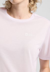 T-shirt di cotone rosa chiaro con collo rotondo e maniche corte. Presenta un logo Jack Wolfskin discreto sul petto. Texture morbida, design semplice.