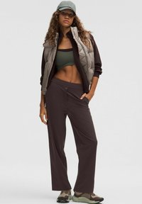 Sportos ruházat világosszürke puffervállal, sötétbarna felsővel és nadrággal. A modellen olívazöld, mintás dizájnú sportcipők vannak.