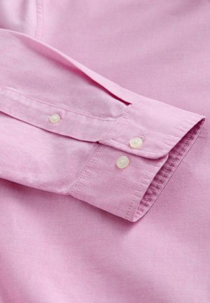 Rosa bomullsskjorta, detaljerad närbild av manschetten med två vita knappar och synlig textur, som visar slät tyg och snygg sömnad.