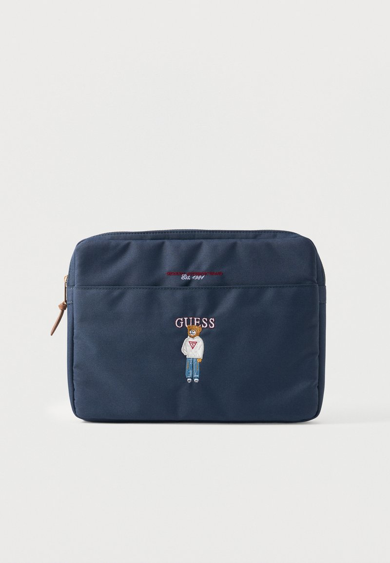 Pochette bleu marine avec zip, ours brodé portant un pull et un jean, et texte « GUESS » au centre devant.