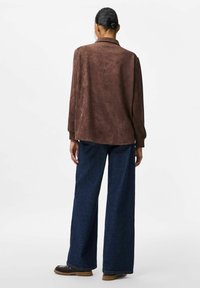 Brun mocka oversized skjorta med krage och långa �ärmar, i kombination med vida mörkblå denimbyxor. Enkel design utan synliga mönster.