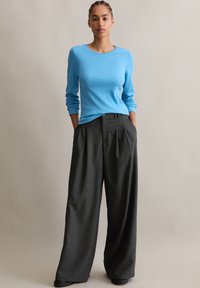 Lichtblauwe lange mouwen top gecombineerd met donkergrijze wijde broekspijpen. De stof lijkt glad, met subtiele stikdetails en zakken.